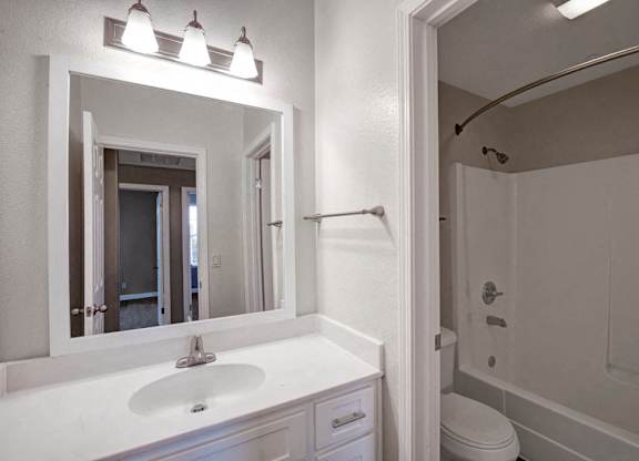 A white bathroom with a sink, mirror, and toilet.