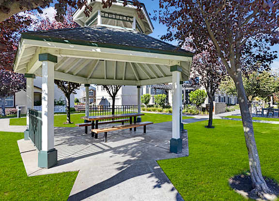 A gazebo with a bench is surrounded by a green lawn.