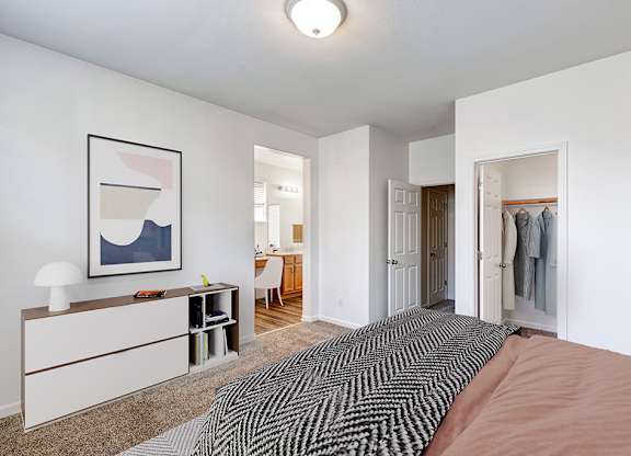 A bedroom with a bed, a desk, and a painting on the wall.
