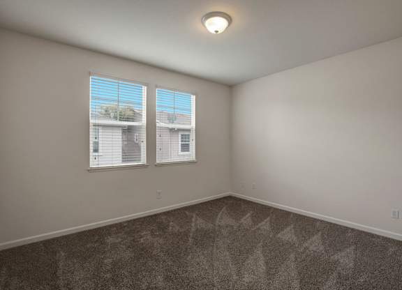 A room with a carpeted floor and two windows.
