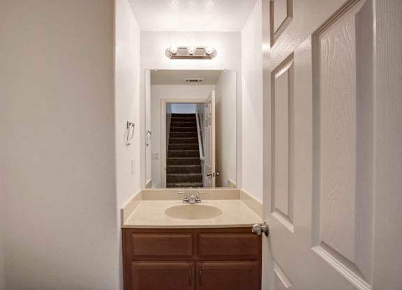 A bathroom with a sink, toilet, and a staircase in the background.