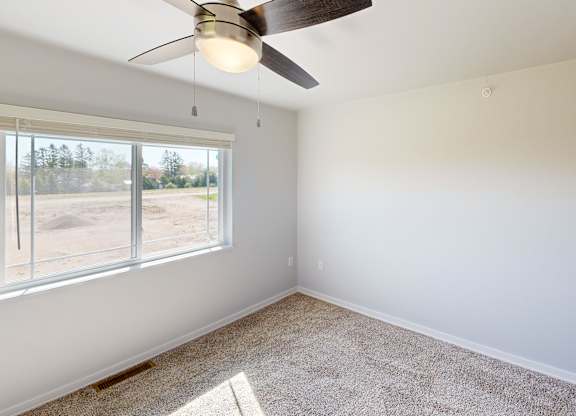 A room with a ceiling fan and a window overlooking a parking lot.