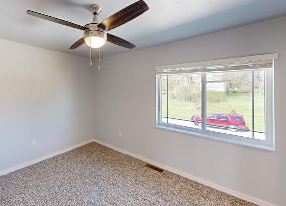 A room with a ceiling fan and a window showing a red car outside.