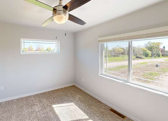 A room with a ceiling fan and two windows.