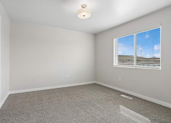 A room with a carpeted floor and a window with blinds.