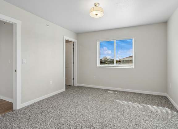 A room with a carpeted floor and a window showing a blue sky with clouds.