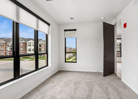 A room with a carpet floor, a door, and a window overlooking a street.