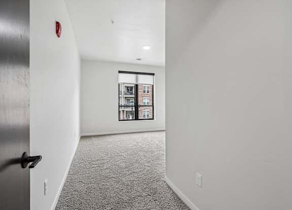 A hallway with a black door and a window with a view of a building.
