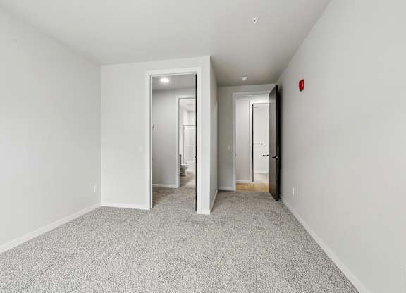 A hallway with white walls and carpeted floors leading to two doors.