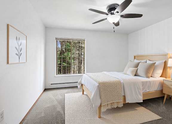 A bedroom with a bed, a ceiling fan, and a window with a view of trees.