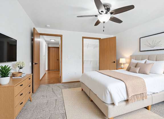 A bedroom with a large bed, a ceiling fan, and a TV on the wall.