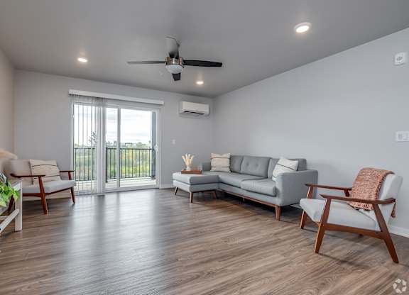 A living room with a grey sofa, wooden chairs, and a ceiling fan.
