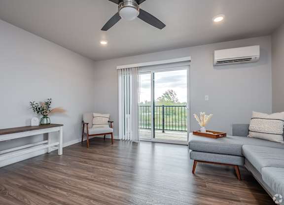 A living room with a grey sofa, a wooden table, a ceiling fan, and a sliding glass door leading to a balcony.
