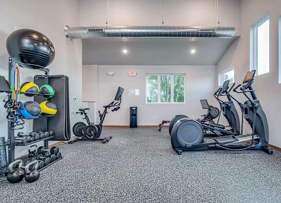 A gym with a variety of equipment including a stationary bike, a rowing machine, and a weight rack.