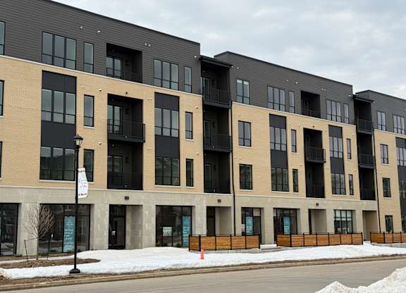 Apartment building with black and beige exterior and snow on the ground.