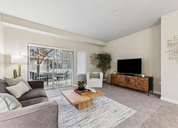 A living room with a grey couch, a wooden coffee table, a flat screen TV and a large window.