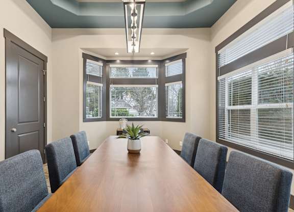 A long brown table is surrounded by grey chairs in a room with a large window.