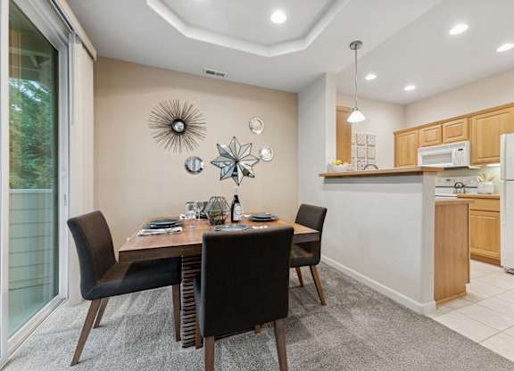 A modern dining room with a table set for two and a kitchen in the background.