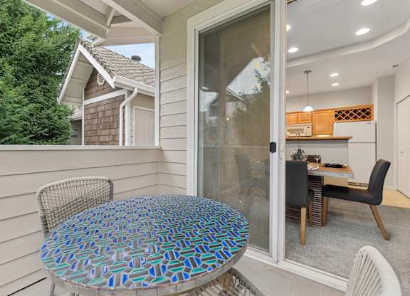 A table with a blue and green patterned top is on a porch.