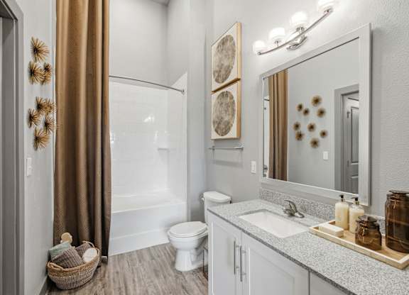 A bathroom with a white toilet, a sink, a mirror, and a shower.
