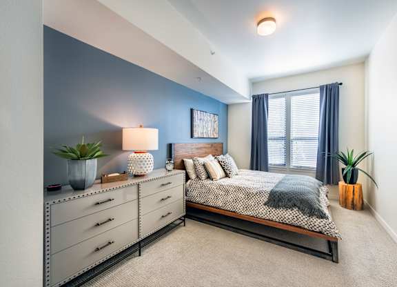 A bedroom with a bed, nightstand, and a plant.