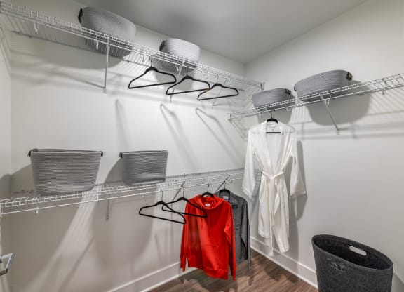 a walk in closet with two wire racks and a white robe and a red jacket