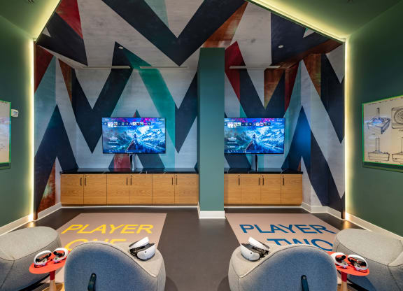 a gaming room with two chairs and two televisions on the wall