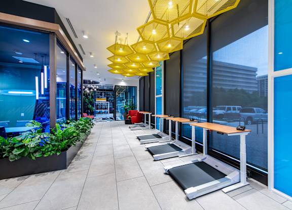 A gym with treadmills and a row of yellow hanging lights.