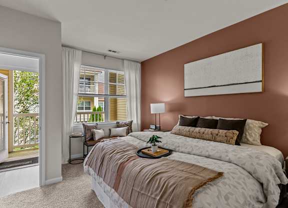 A bedroom with a large bed and a window overlooking a balcony.