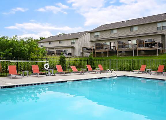 A swimming pool in front of a building with red chairs around it.