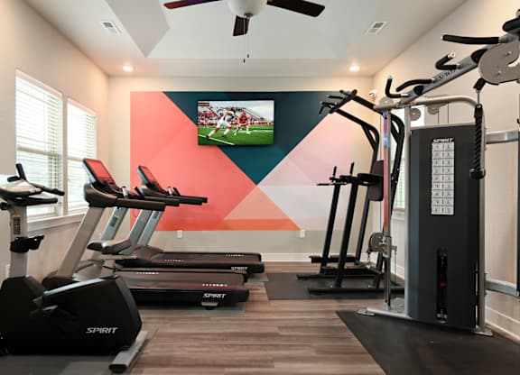 A gym with treadmills, elliptical machines, and a television playing a football game.