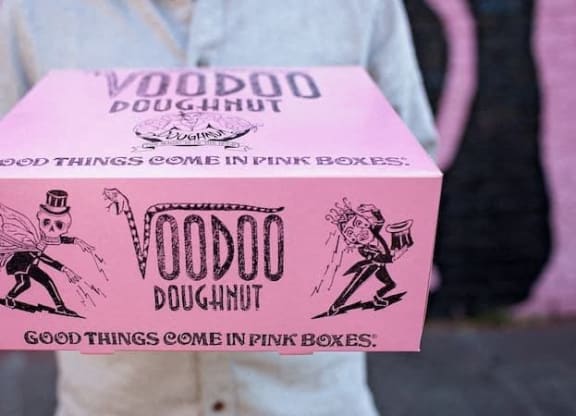 a person holding a pink box that says voodoo doughnut