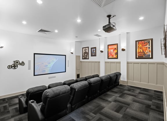 a theater room with a row of black chairs and a tv on the wall