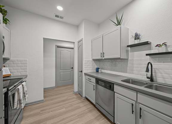 A modern kitchen with a white color scheme and wooden flooring.