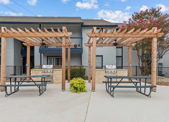 a picnic area with two picnic tables and a barbecue grill in front of a building