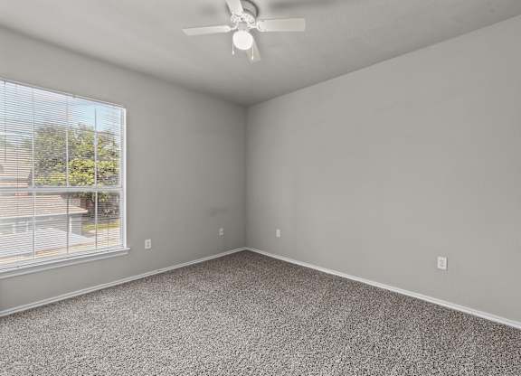 A room with a ceiling fan and a window overlooking a fence.