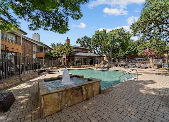 A pool with a fountain in the middle of a brick patio.