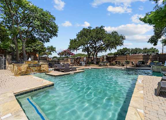 A large outdoor swimming pool surrounded by trees and lounge chairs.