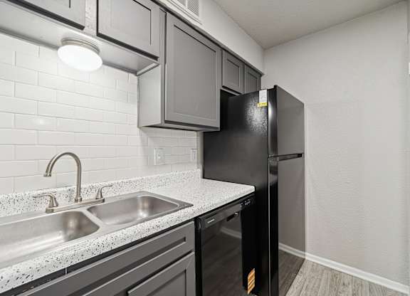 A kitchen with a black fridge and a white tiled backsplash.
