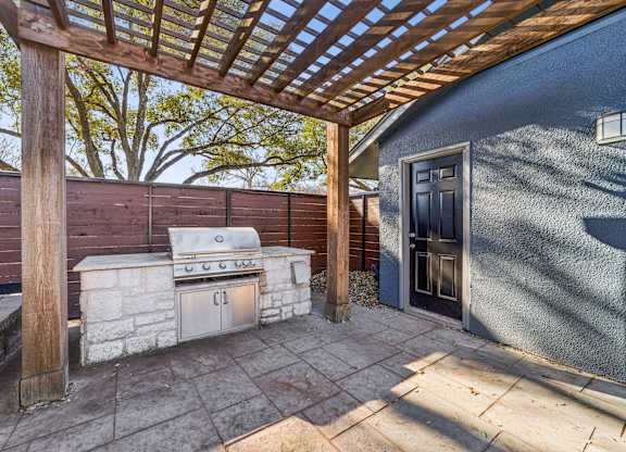 A patio with a grill and a pergola.