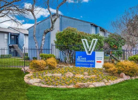 a round flower bed with yellow flowers in front of a blue building with a sign that says