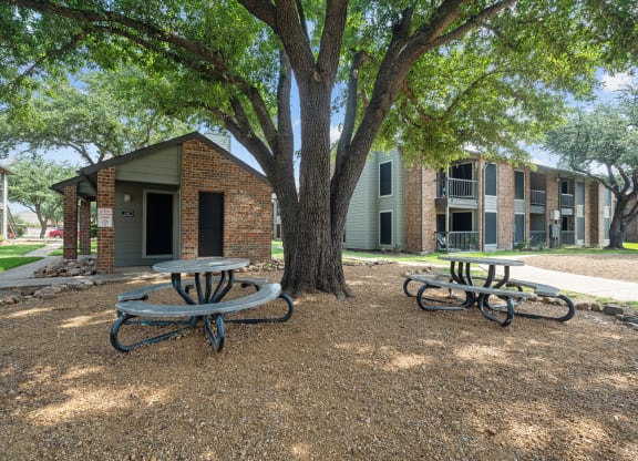a picnic area with two tables and a tree in front of a brick building