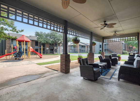 a covered patio with furniture and a playground in the background