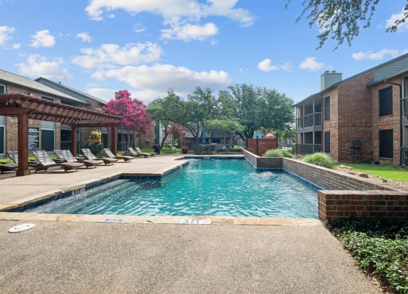 a swimming pool with lounge chairs and trees in the background