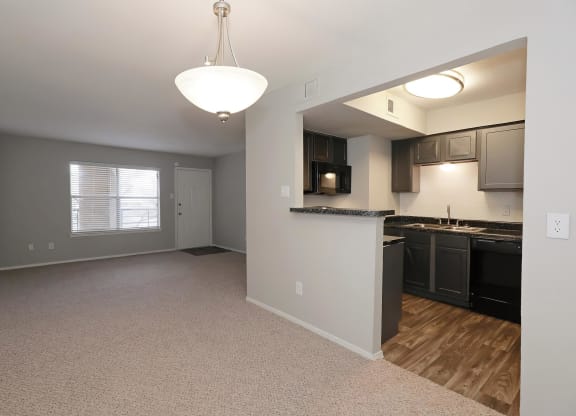 an empty living room with a kitchen in the background