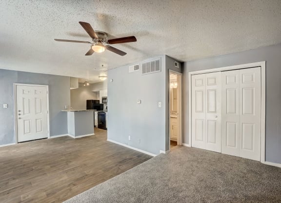 an empty living room with a ceiling fan and a kitchen