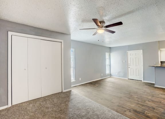 an empty living room with a ceiling fan and a door to the kitchen