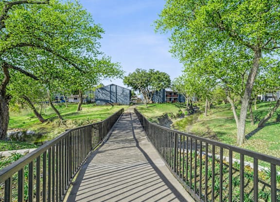 A wooden walkway with metal railings leads through a lush green park.