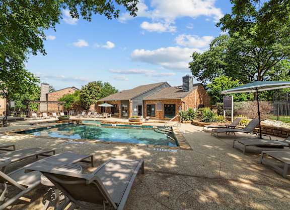 A pool surrounded by lounge chairs and trees.