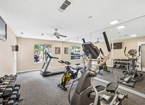 A gym with a variety of exercise equipment including treadmills, stationary bikes, and weight machines.